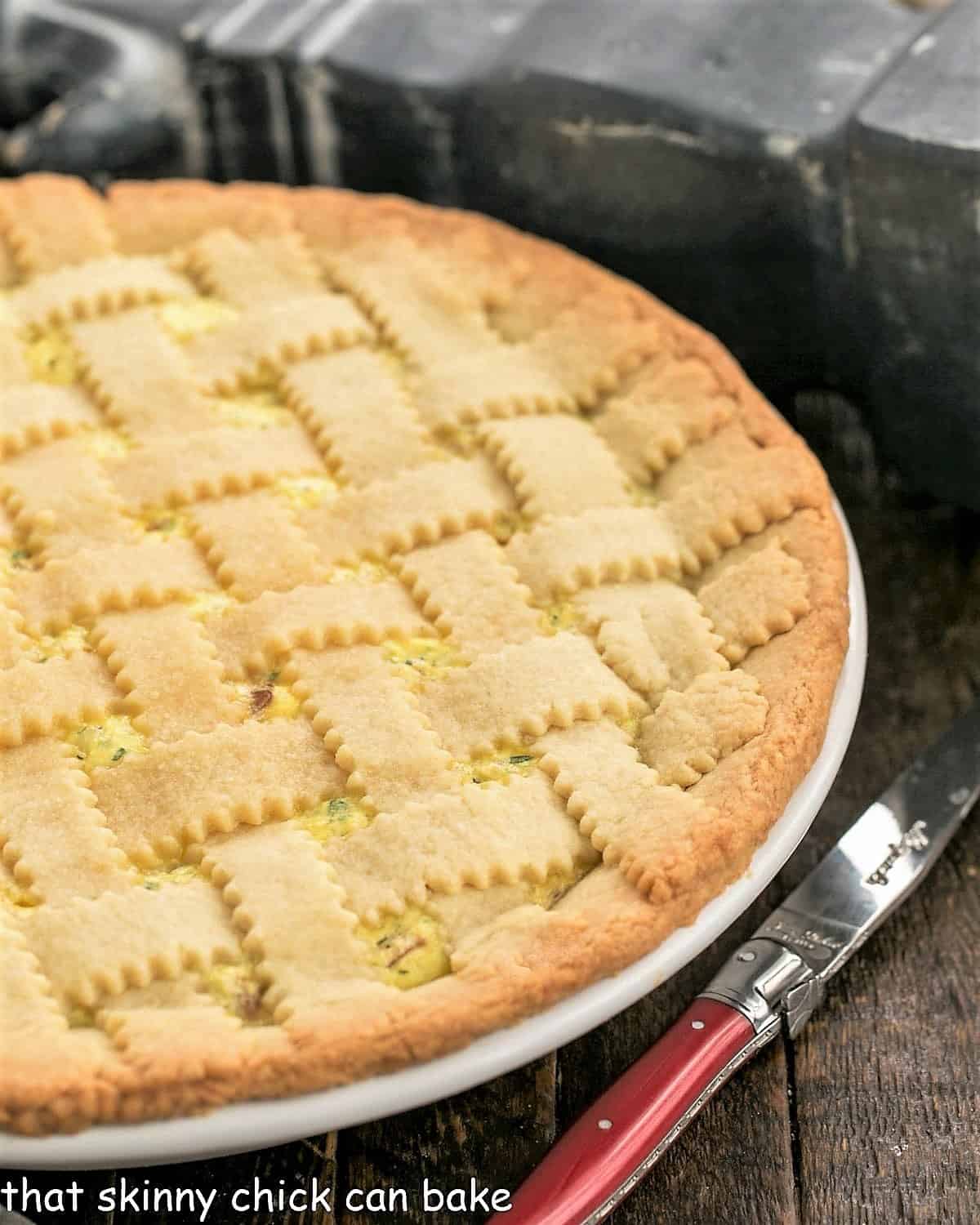 Close view of uncut pizza rustica in a white ceramic pie plate with a red handle knife.