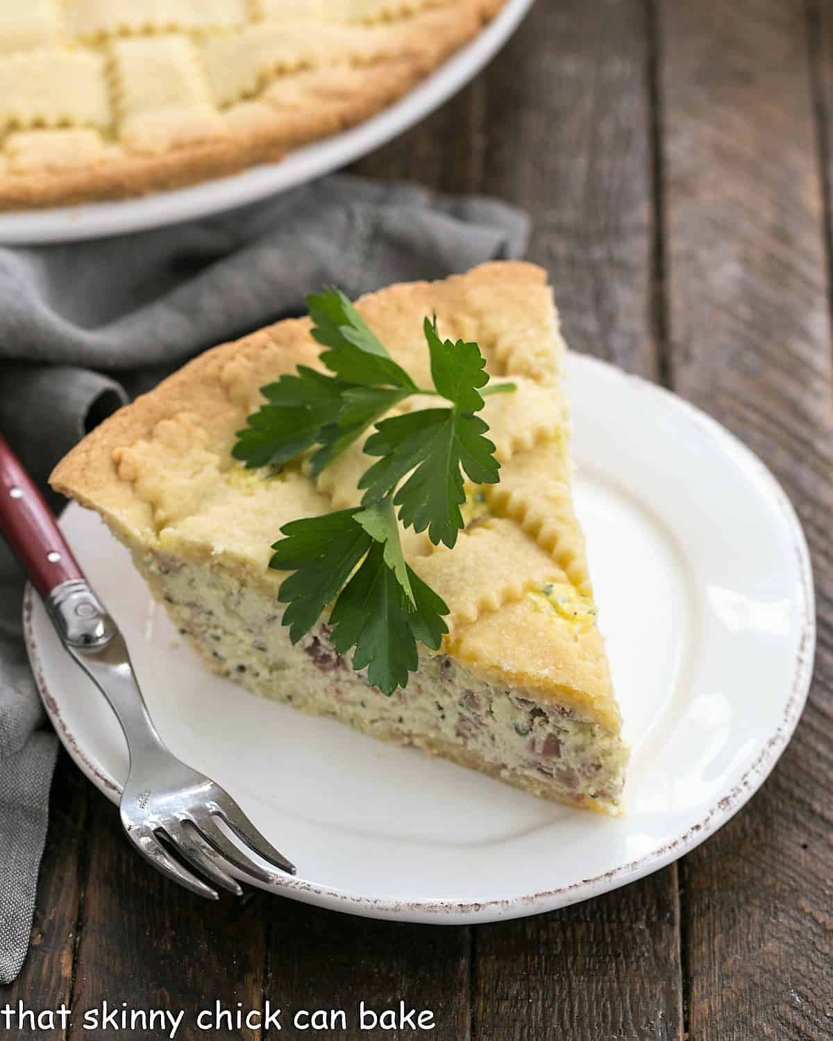 Slice of pizza rustica on a white plate with a parsley sprig on top.