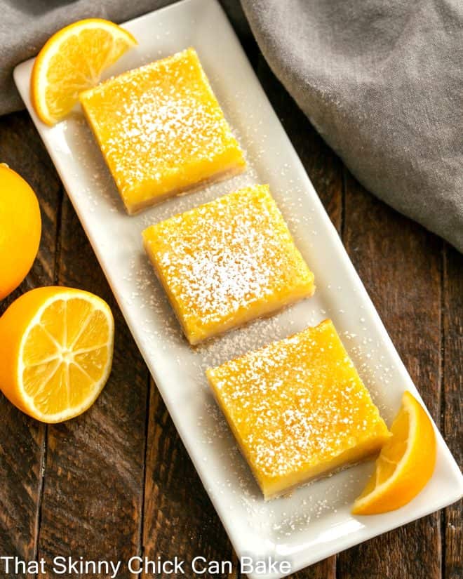 Overhead view of a tray of 3 meyer lemon bars with small lemon slices to garnish