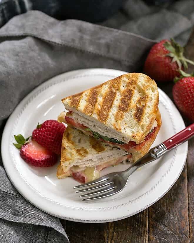 Strawberry, Turkey and Brie Grilled Cheese stacked on a white lunch plate with a red handled fork.