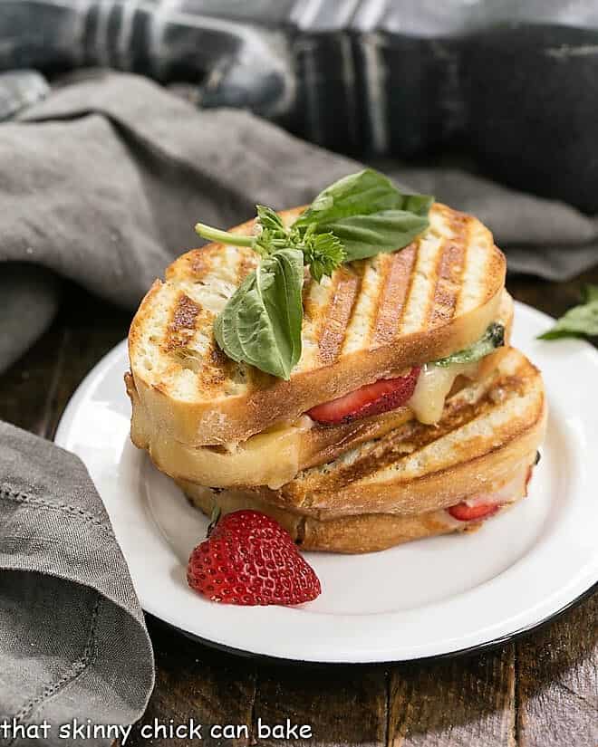 Strawberry, Turkey and Brie Grilled Cheese halves stacked on a round white plate with basil and strawberry garnish.