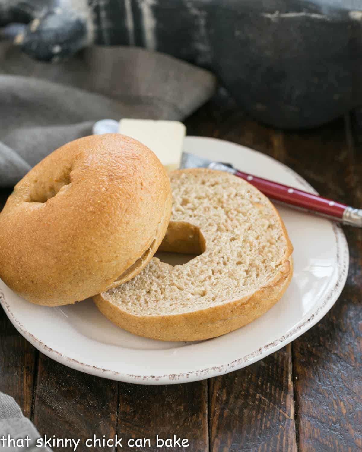 Sliced whole wheat bagel on a round white plate with a red handle knife.