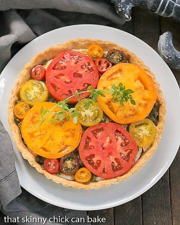 Overhead view of a Fresh Tomato Tart on a serving plate garnished with herbs