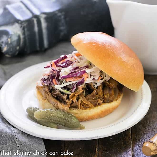 Pulled Pork Sandwich on a bun topped with coleslaw with a pitcher of BBQ sauce