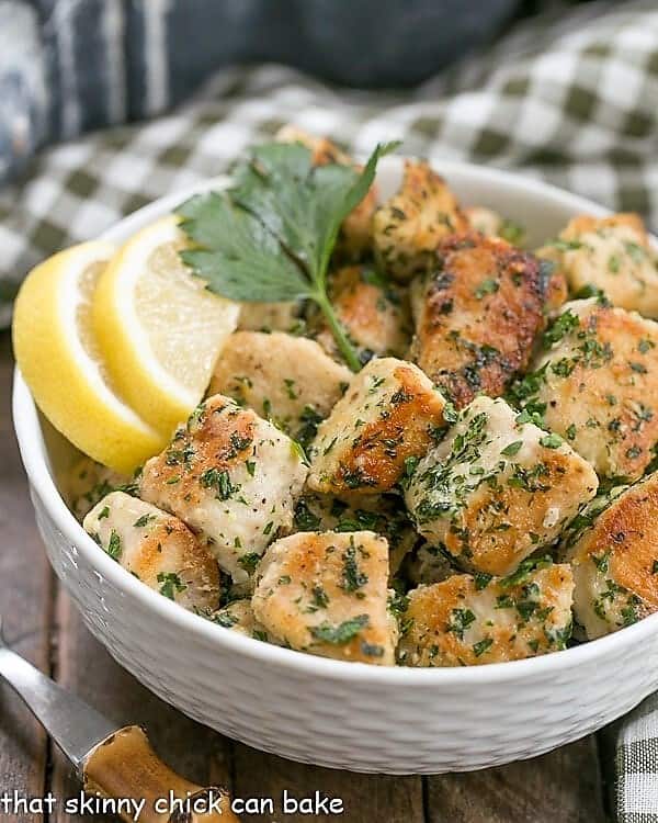 Chicken with Garlic and Parsley in a white basket weave bowl garnished with lemons and a sprig of parsley.