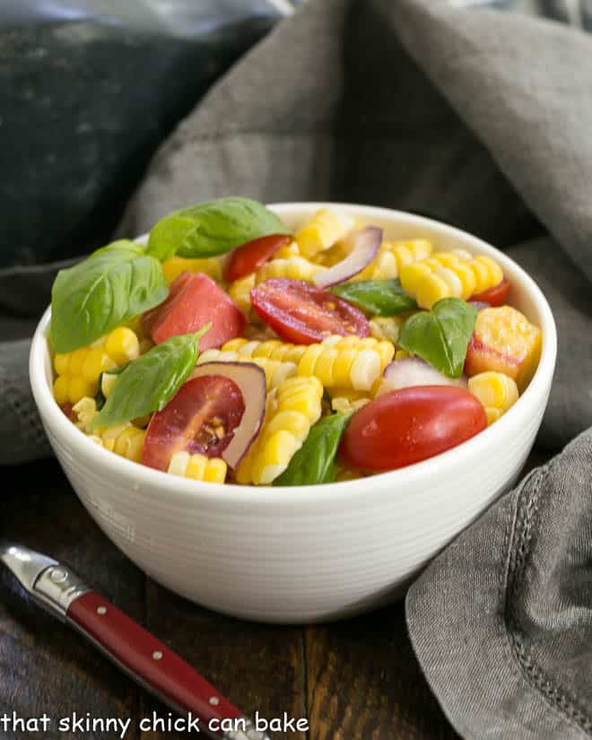Small bowl of fresh corn basil and tomato salad with a red handle fork.