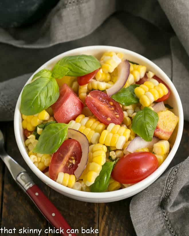 Small white bowl filled with corn, tomato and basil salad