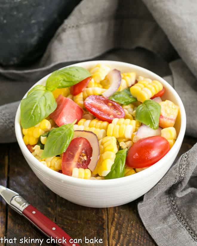 Small white bowl filled with fresh corn, basil and tomato salad