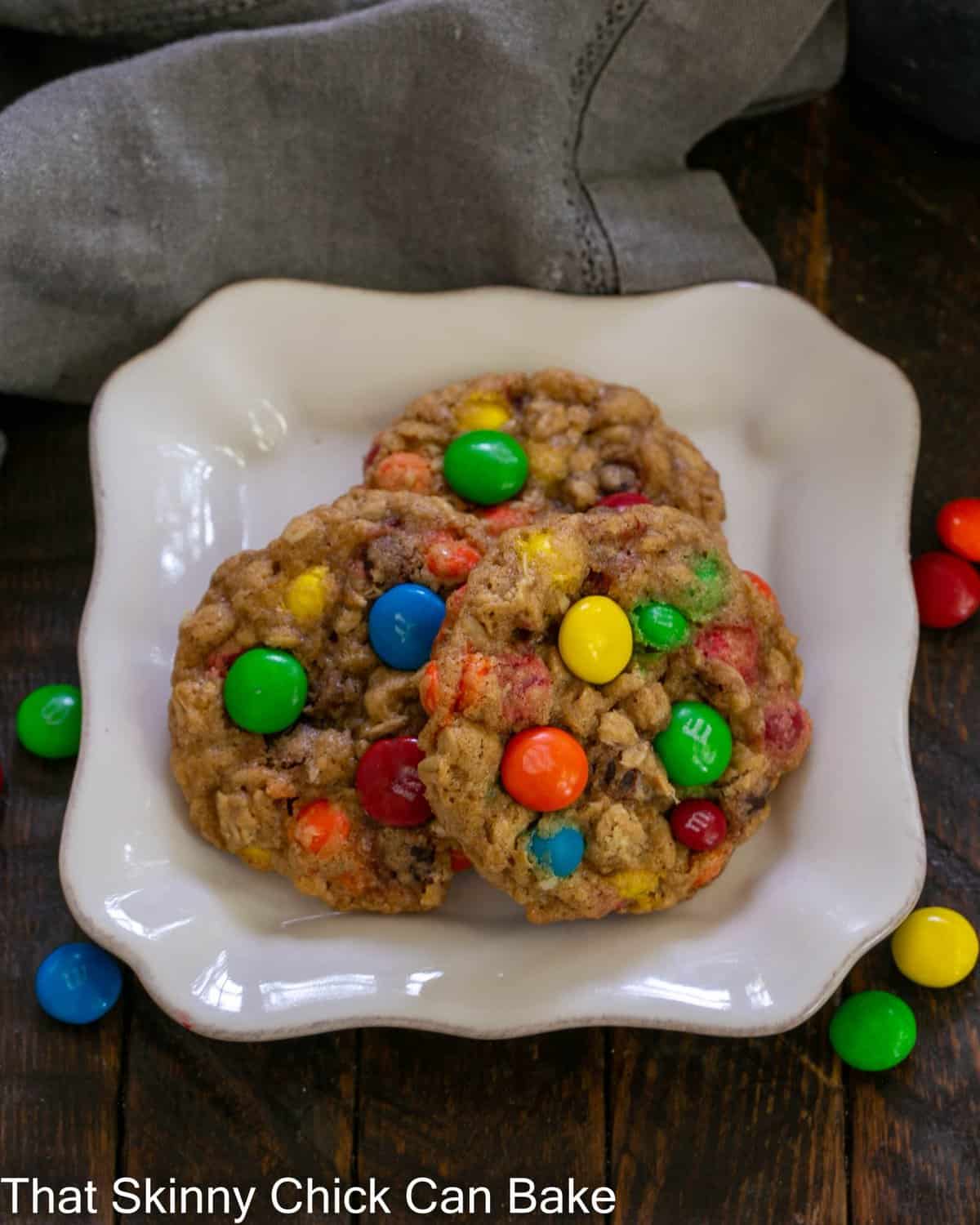 Overhead view of 3 oatmeal M & M cookies on a square white plate.