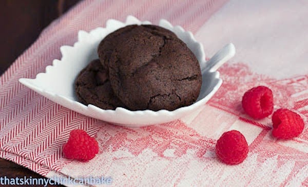 A close up of cookies and cream cookies in a white leaf bowl with raspberries surrounding it