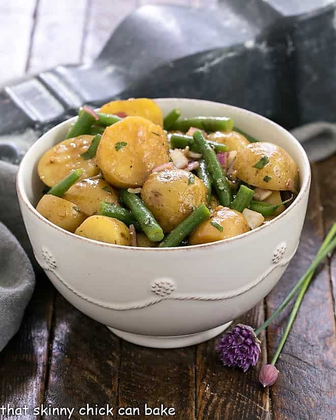 Homemade potato salad with green beans in a white serving bowl.