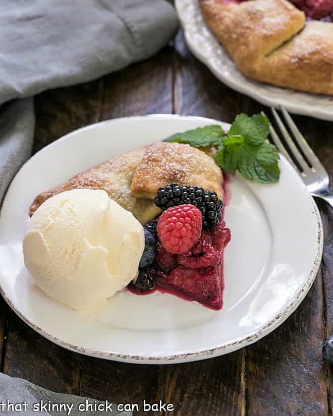 Slice of berry galete on a round white plate with a scoop of vanilla ice cream.