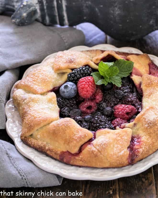 Mixed berry galette with a sprig of mint on a decorative white serving plate