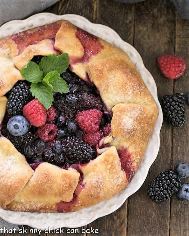 Overhead view of a rustic berry tart on a white plate surrounded by fresh berries.