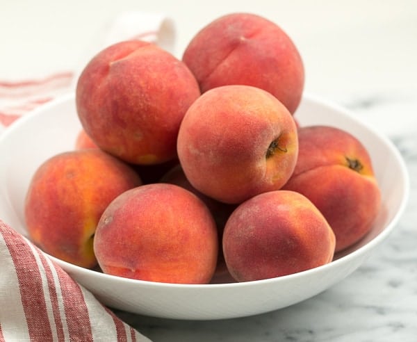 A white bowl full of red haven peaches.