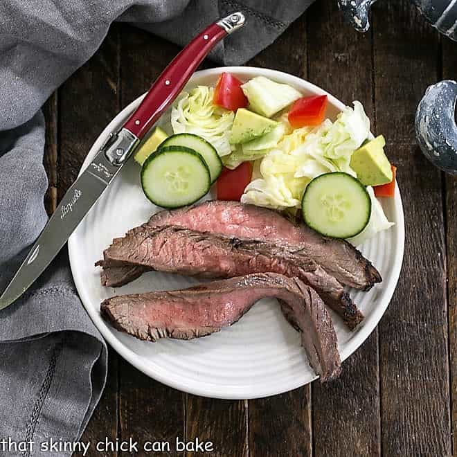 Overhead view of marinated flank steak slices on a white plate with a side of tossed salad