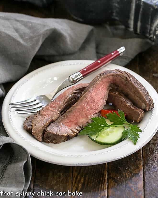 Slices of flank steak on a white plate with a red handled fork.