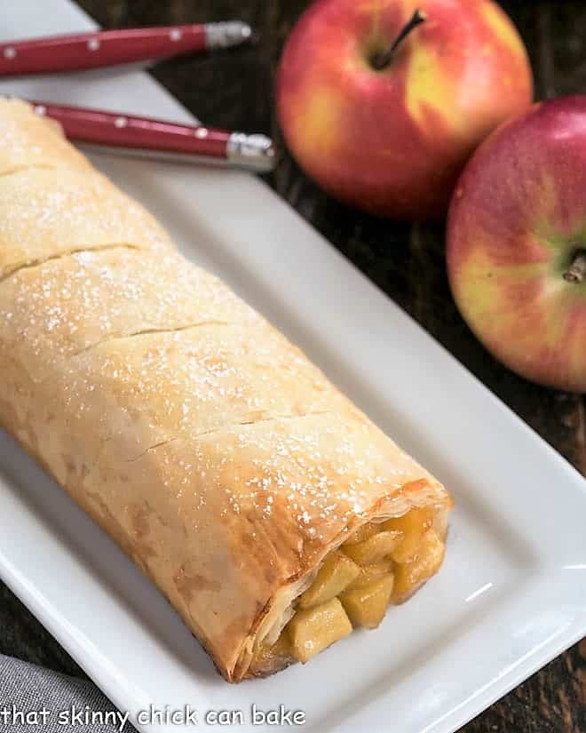 Apple Strudel dusted with powdered sugar on a white platter