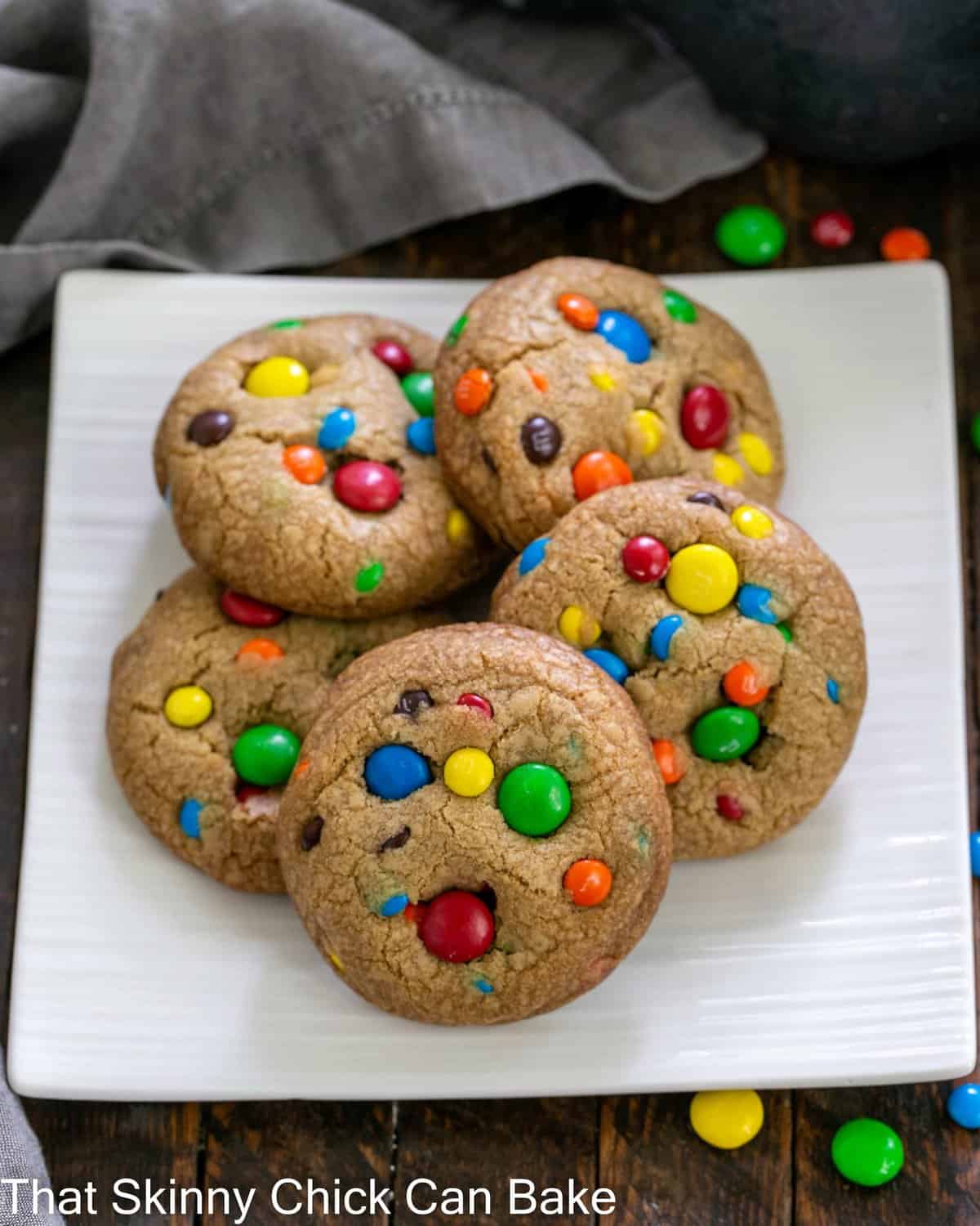 Overhead view of 5 M&M cookies on a square white plate.