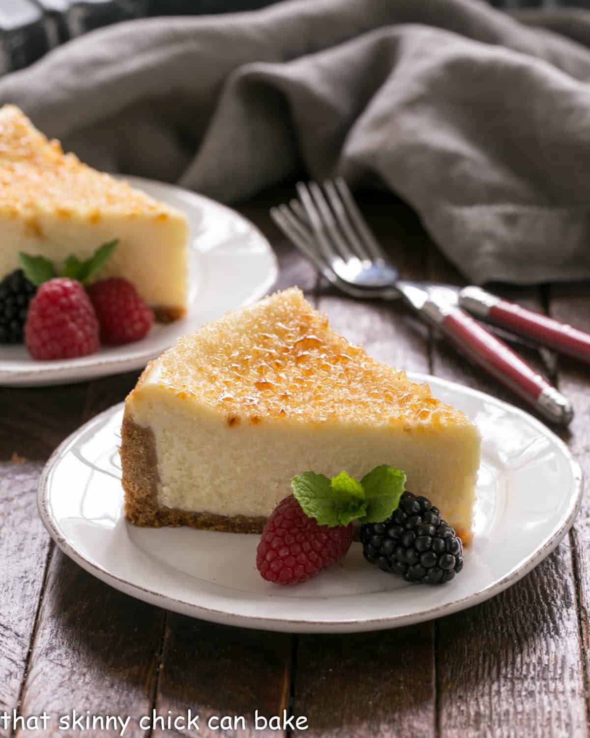 Two slices of creme brulee cheesecake on white plates with berry garnish.