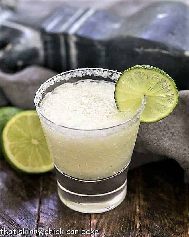 A beer margarita in a high ball glass with a salted rim and thin lime slice garnish