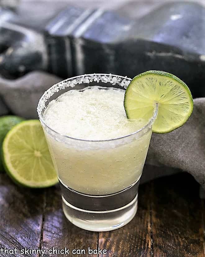 A beer margarita in a high ball glass with a salted rim and thin lime slice garnish.