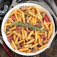 Overhead view of Creamy Italian Sausage Pasta with a sprig of rosemary in a white serving bowl