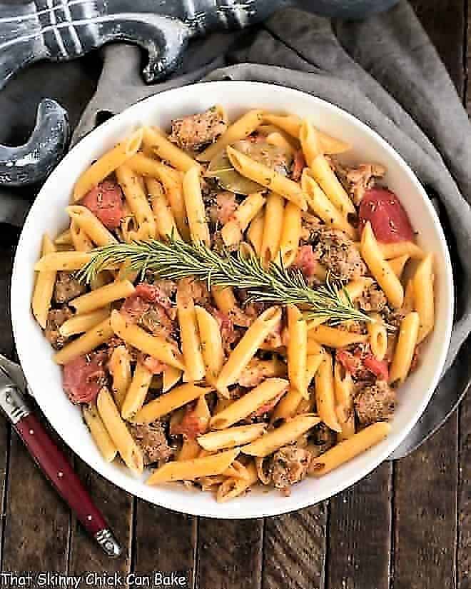 Overhead view of Creamy Italian Sausage Pasta with a sprig of rosemary in a white serving bowl
