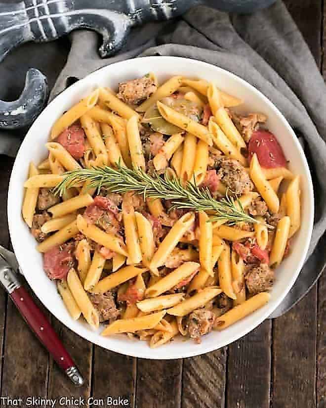 Creamy Italian Sausage Pasta with a sprig of rosemary in a white serving bowl