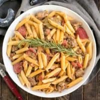 Creamy Italian Sausage Pasta with a sprig of rosemary in a white serving bowl