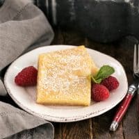 Two gooey butter bars on a round white plate with fresh raspberries and mint