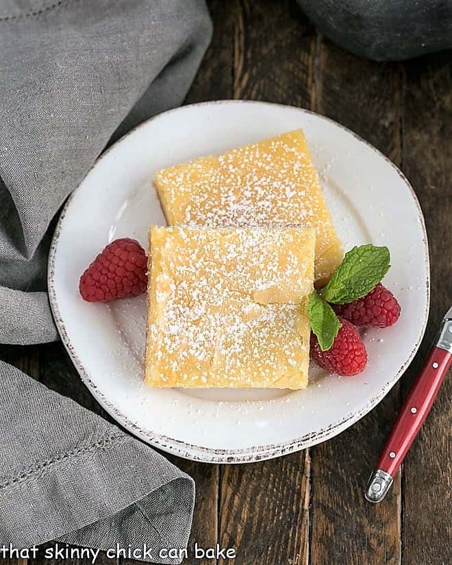 Overhead view of gooey butter cake slices on a white plate with raspberries.