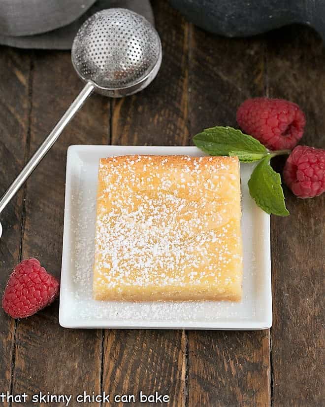 One slice of gooey butter cake on a square white plate with a powdered sugar duster.