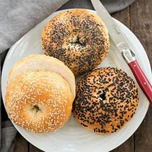Homemade Bagels on a white ceramic plate with a red handled knife
