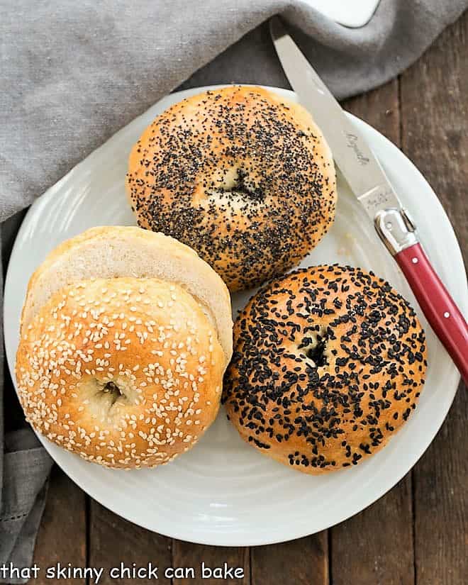 Homemade Bagels on a white ceramic plate with a red handled knife.