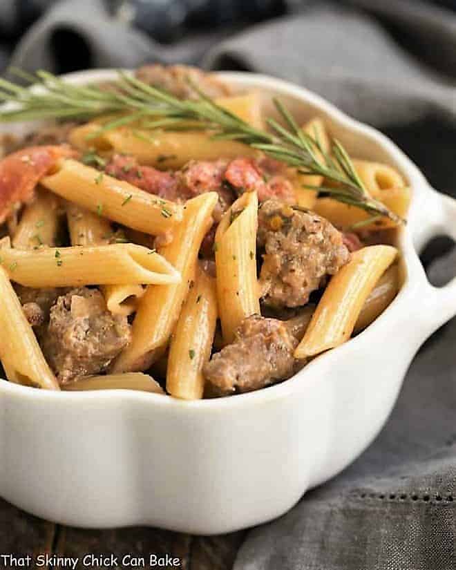 Creamy Italian Sausage Pasta in a white casserole dish garnished with rosemary