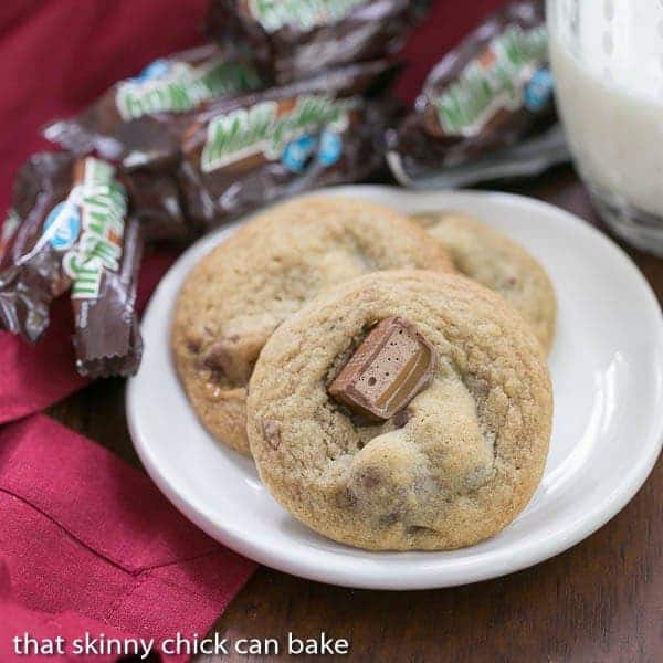 Three Milky Way Cookies on white plate surrounded by empty Milky Way wrappers. 