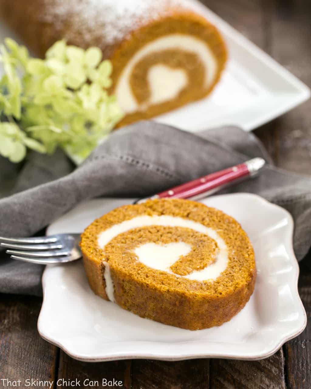 Old Fashioned Pumpkin Roll slice reveals a swirl of cream cheese filling on a white ceramic plate.