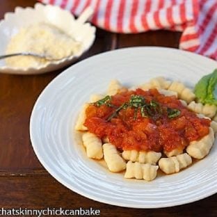 Ricotta Gnocchi topped with marinara and fresh basil on a white dinner plate