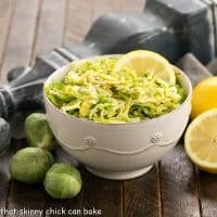 Shredded Brussels sprouts salad in a serving bowl next to a half lemon and 3 brussels sprouts