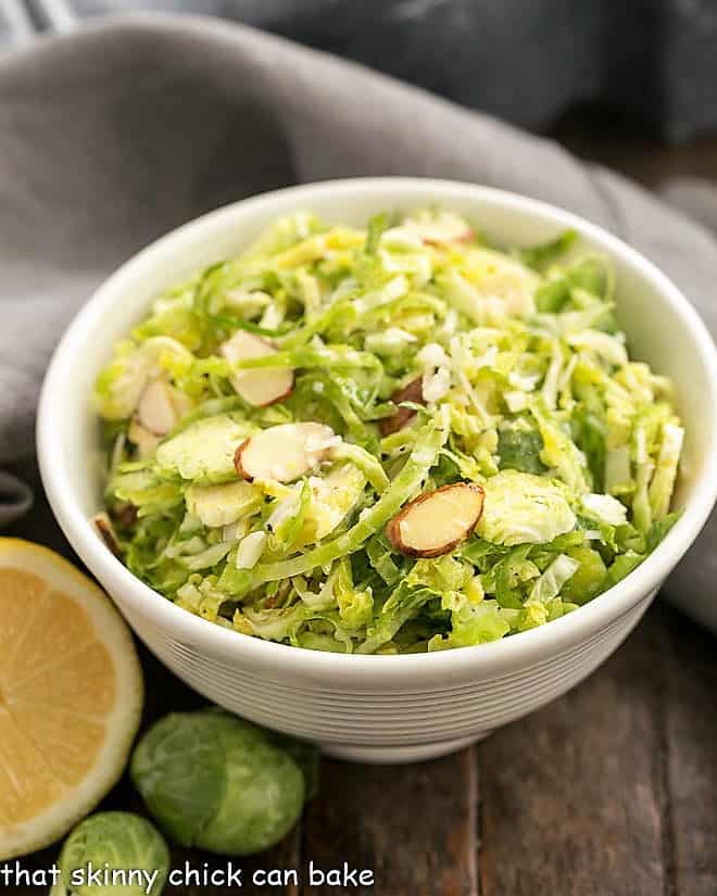 Crisp, refreshing Shaved Brussels Sprouts Salad with a lemony Dijon dressing - a healthy, delicious side dish! #healthy #salad #Brusselssprouts #lemon #almonds #Dijon #thatskinnychickcanbake Shaved Brussels Sprouts Salad in a small white salad bowl