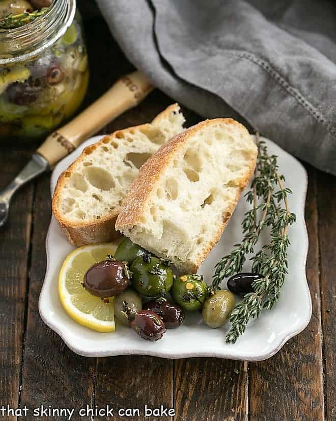 Herbed oives on a white plate with bread and fresh thyme