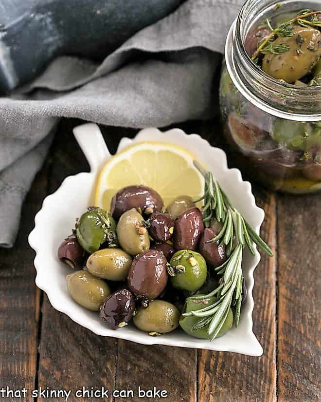 herbed olives in a ceramic leaf plate with a slice of lemon and rosemary