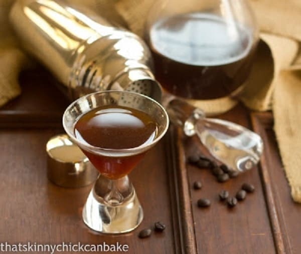 Homemade Kahlua in a glass with a decanter and coffee beans.