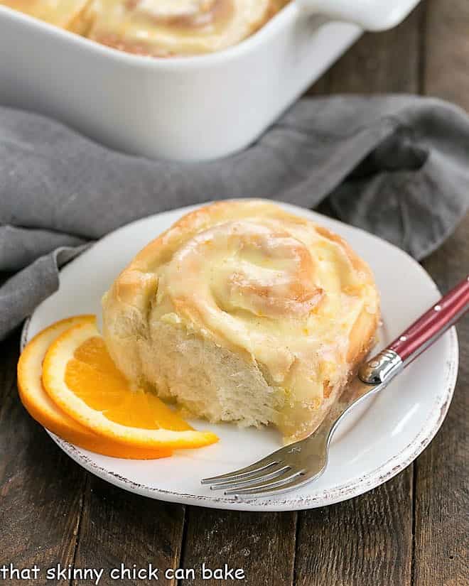 Orange Sweet Rolls in a baking dish with one roll in front on a small plate with a red handled fork