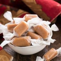 Homemade brown sugar caramels wrapped in wax paper in a white bowl