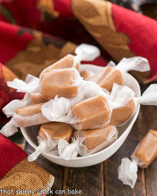 Homemade Caramels wrapped in waxed paper in a white candy bowl.