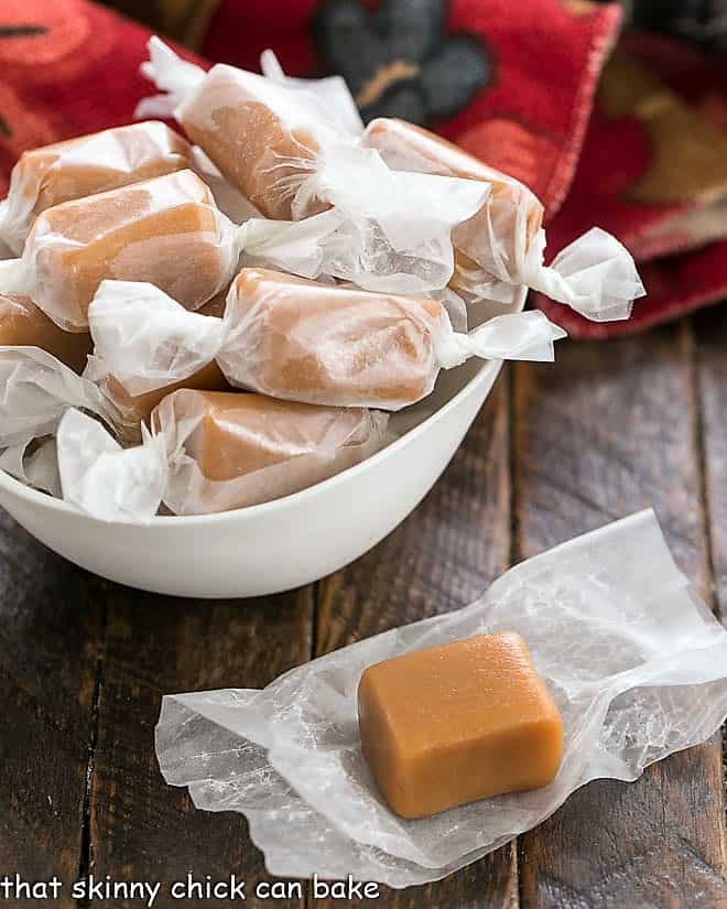 Bowl of wrapped brown sugar caramels with an unwrapped caramel in the foreground.