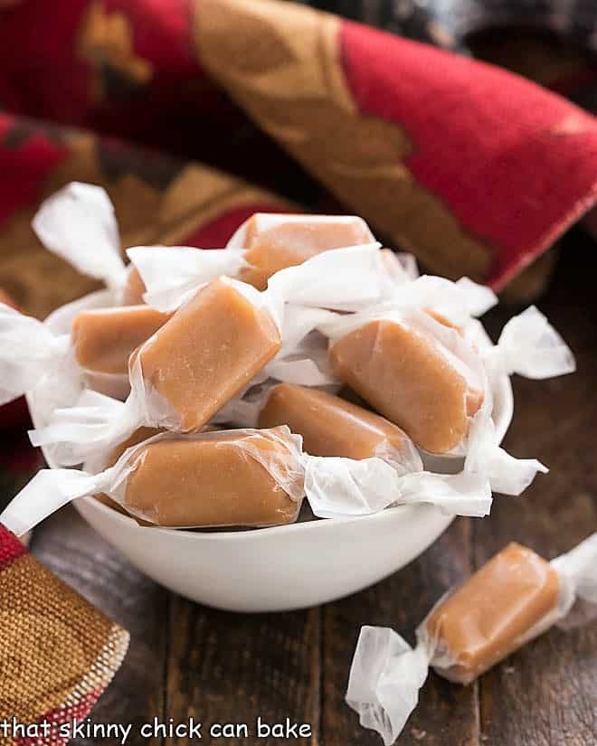 Homemade brown sugar caramels wrapped in wax paper in a white bowl