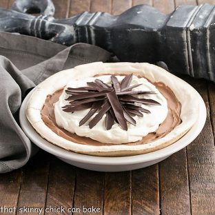 Chocolate Angel Pie topped with whipped cream and chocolate shards in a white pie plate